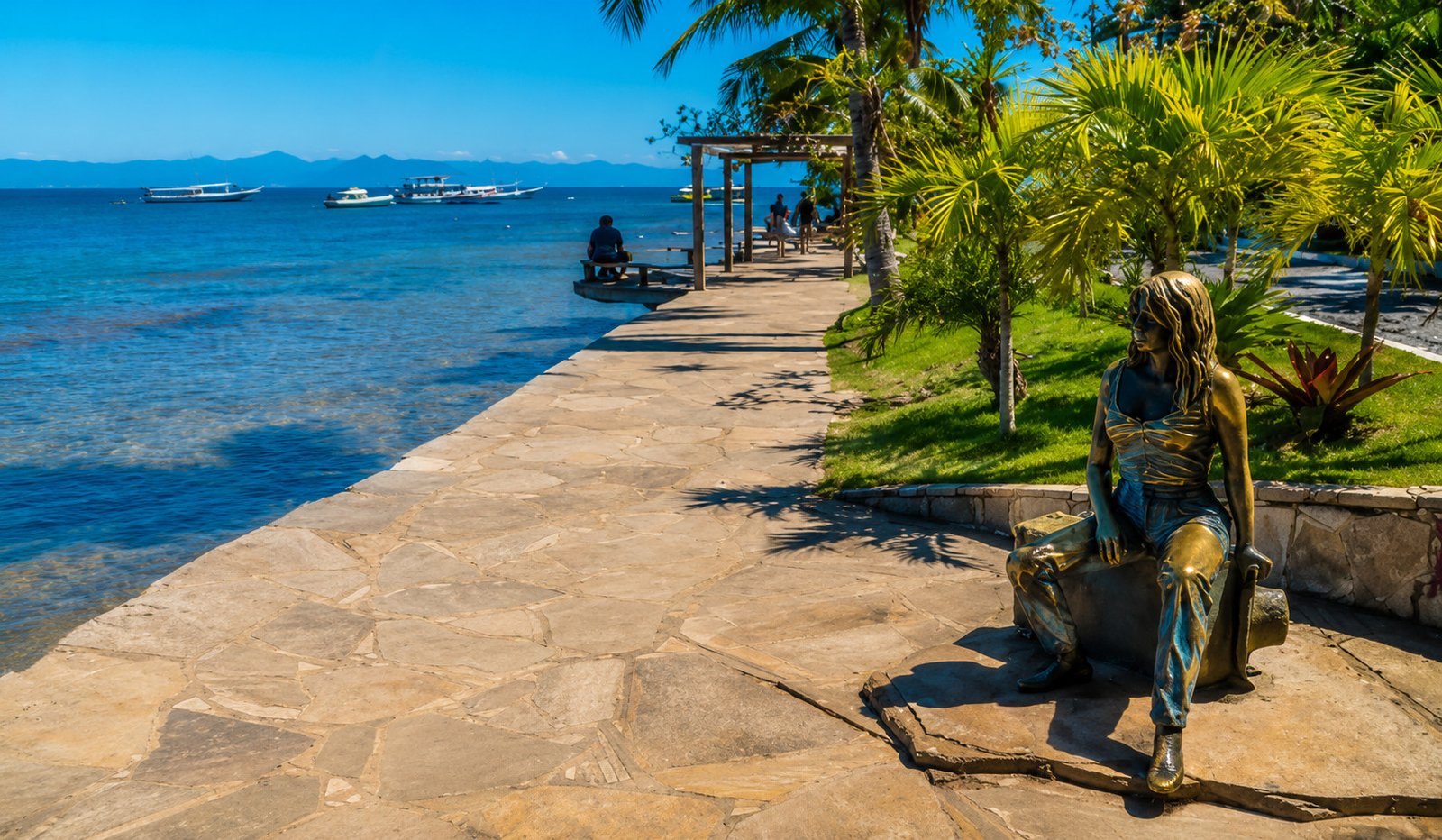 Orla Bardot em Búzios com calçadão à beira-mar, esculturas e barcos